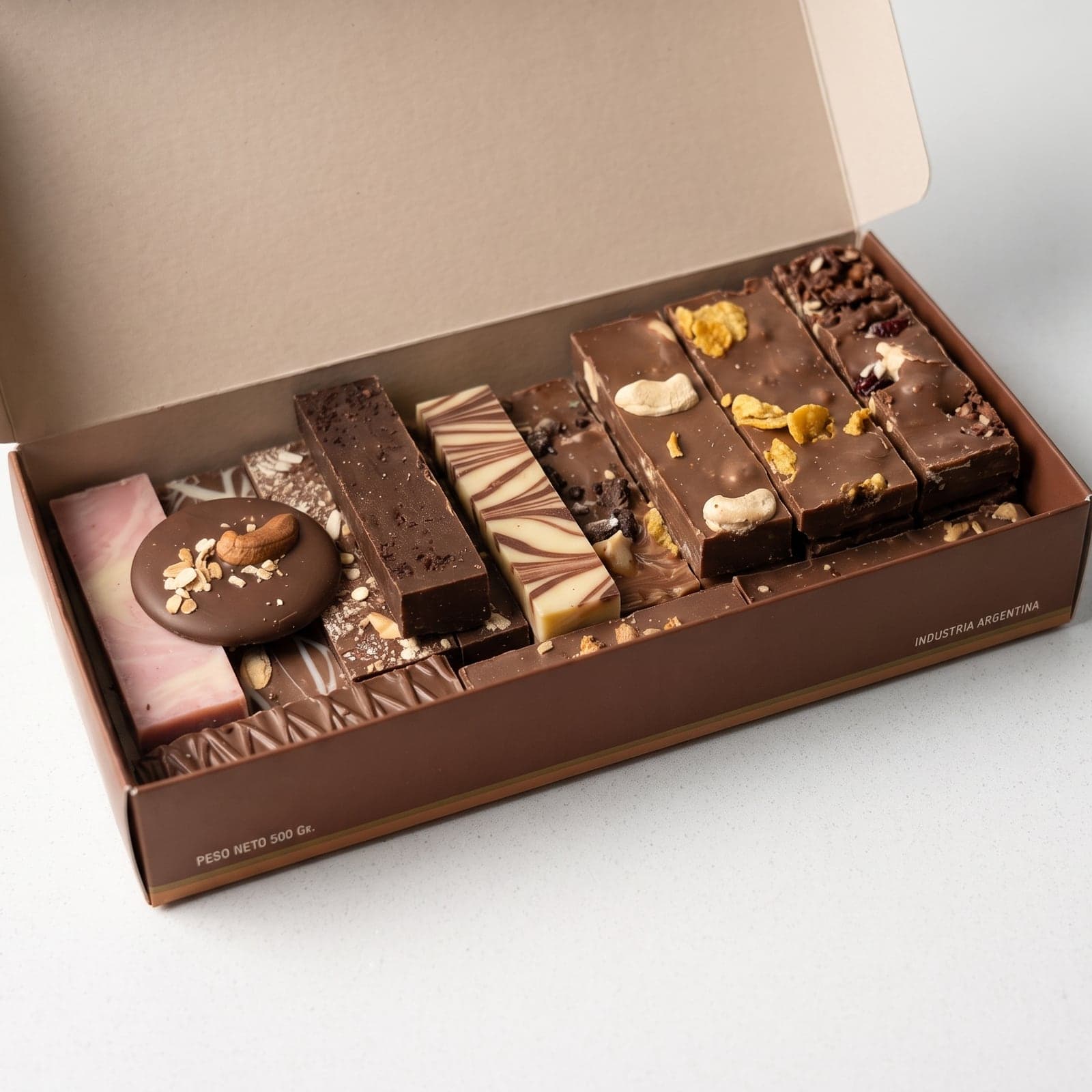 Caja abierta del surtido de chocolates artesanales de 1/2 kg, con barras cortadas a cuchillo y frutos secos a la vista
